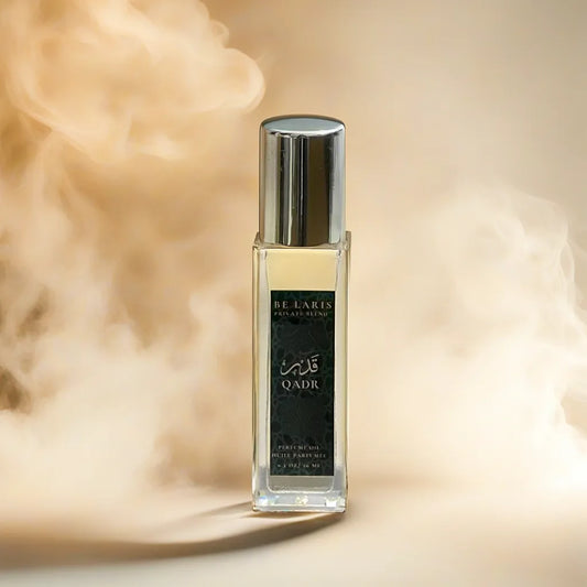 A glass perfume oil bottle with the name Qadr on it against the backdrop of cream smoke and shadows.